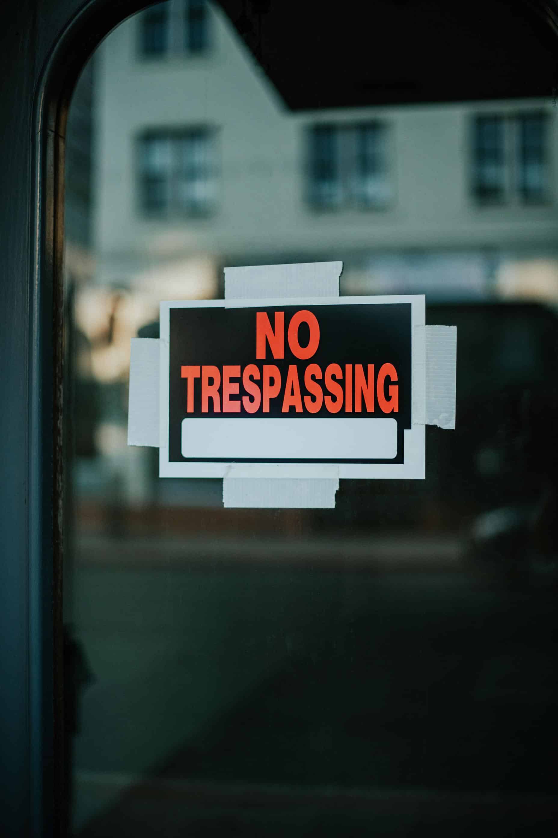 A NO TRESPASSING sign taped up inside a glass door, with the street reflected in the glass