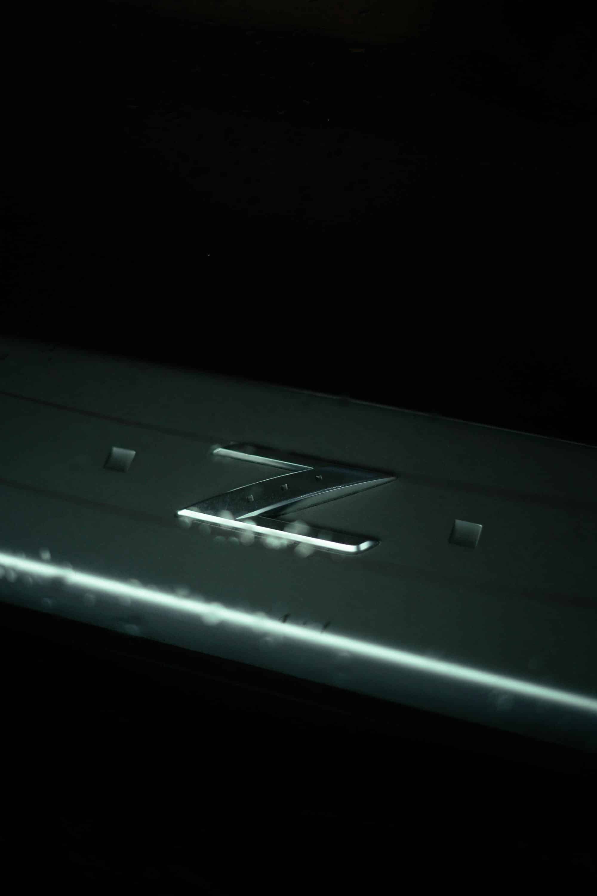 A chrome Z emblem on the dark bodywork of a car, picked out by a single streak of light